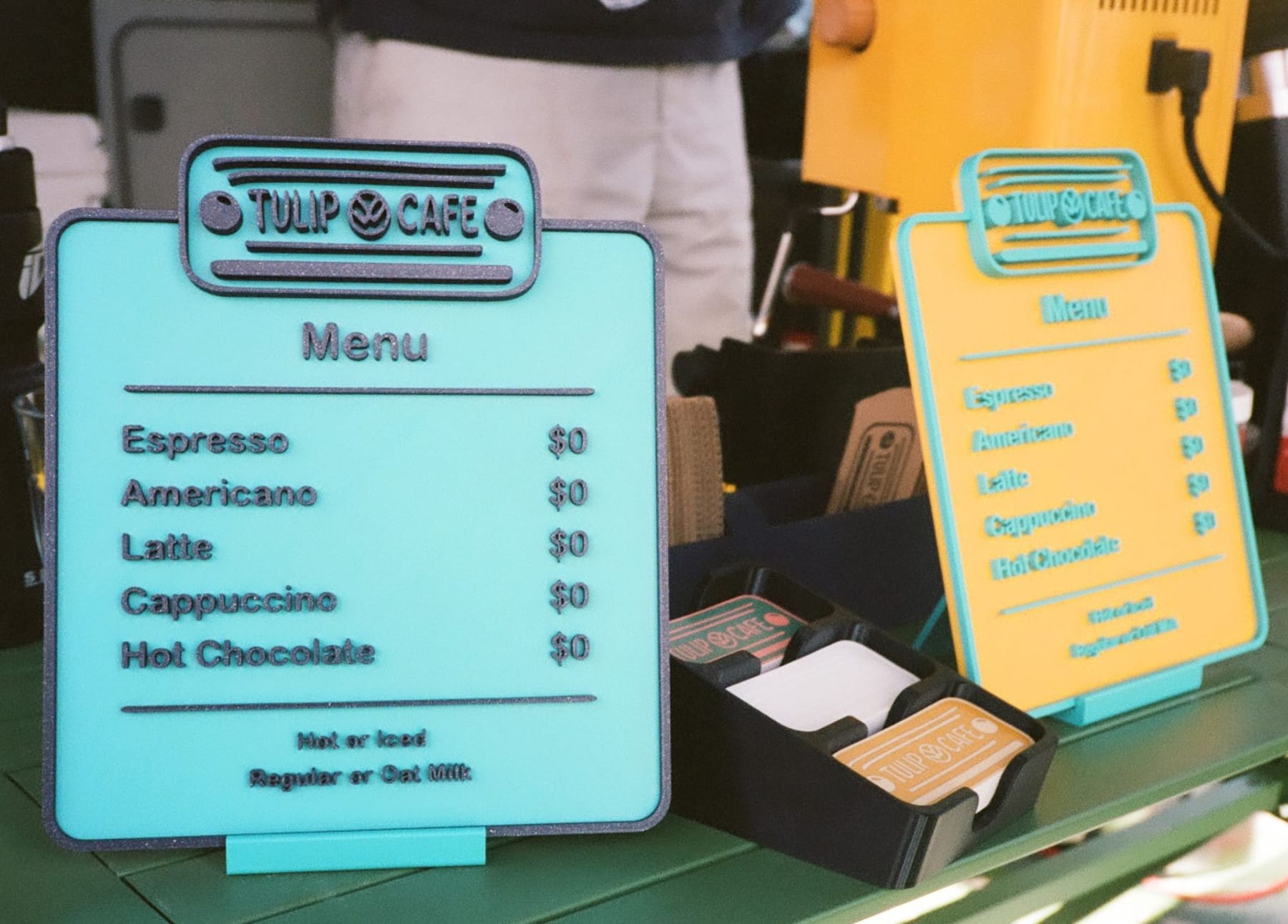 Two 3D-printed Tulip Cafe menu boards listing every drink at $0